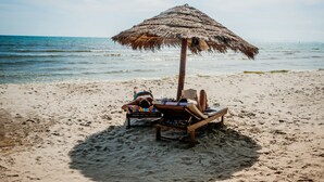 A beach with a thatched umbrella providing shade, two lounge chairs, and a sandy beach. - Spayhiti (Sihanoukville)