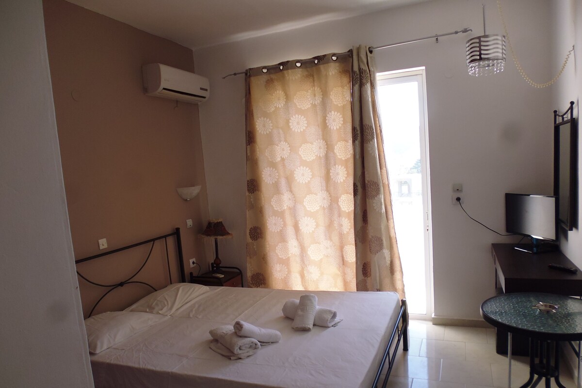 A hotel room with a bed, a desk with a TV, an air conditioner, and a curtain.