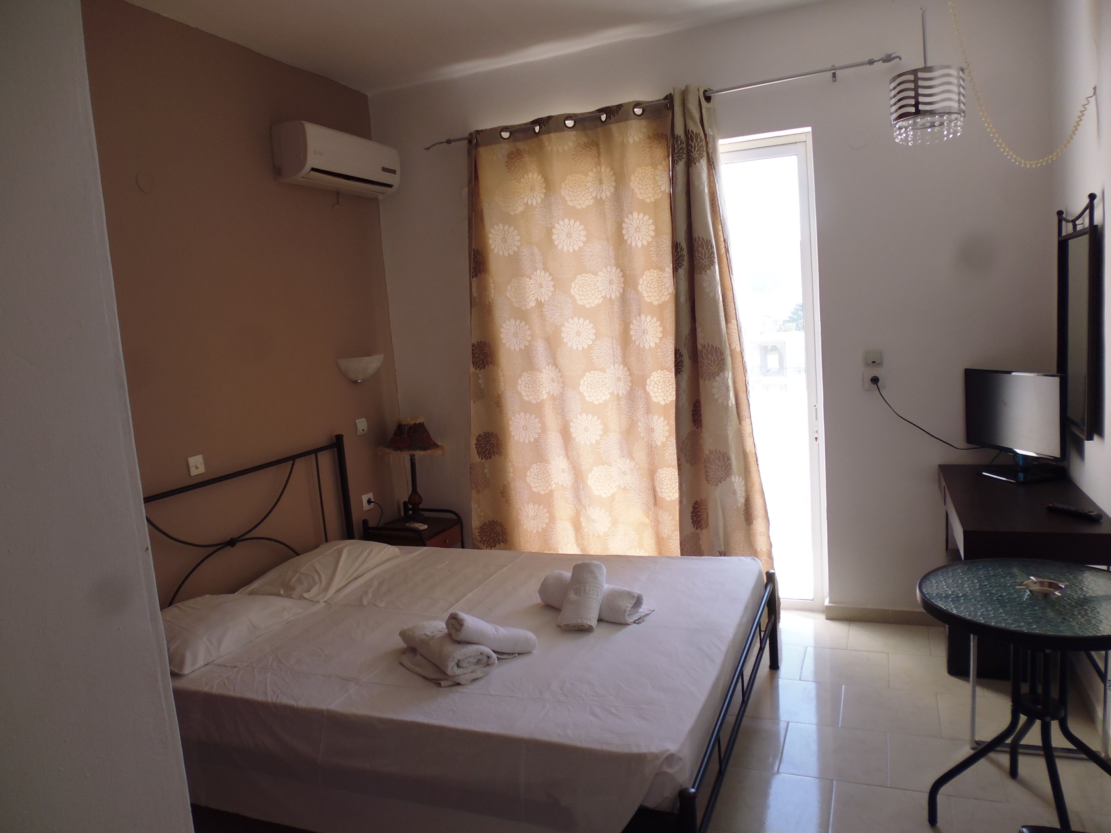 A hotel room with a bed, a desk with a TV, an air conditioner, and a curtain.