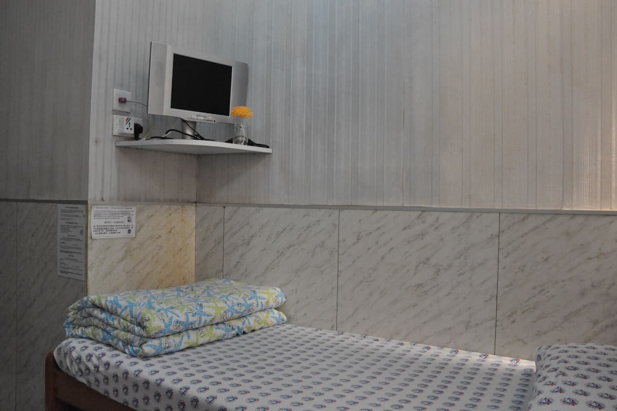 Una habitación con una cama, un pequeño estante con un televisor y un cartel en la pared.