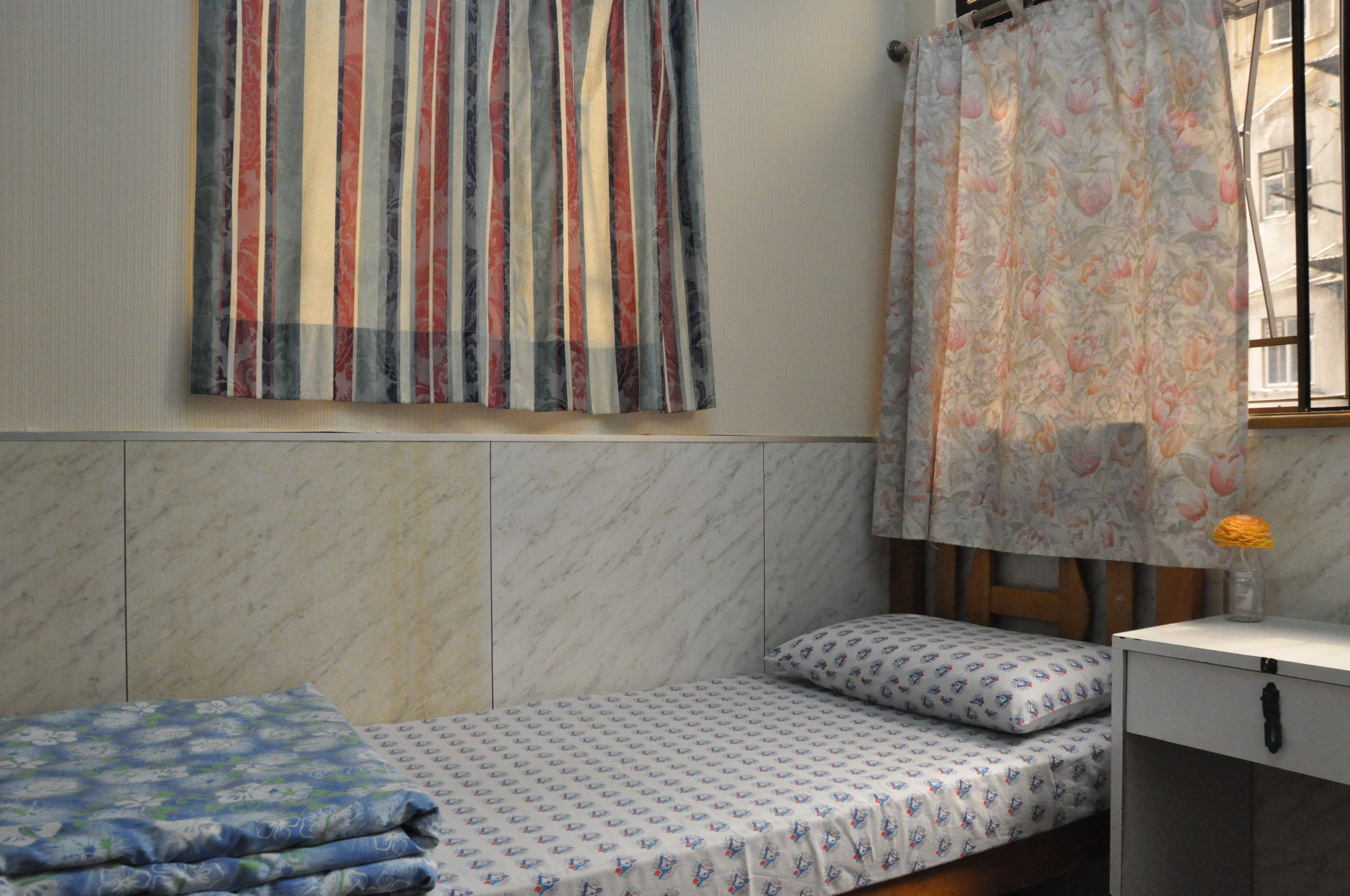 A small, neatly arranged bedroom with a bed, a nightstand, and a window with curtains.