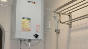 A bathroom with a white water heater, a hand dryer, and a towel rack. - DormHK (Kowloon)