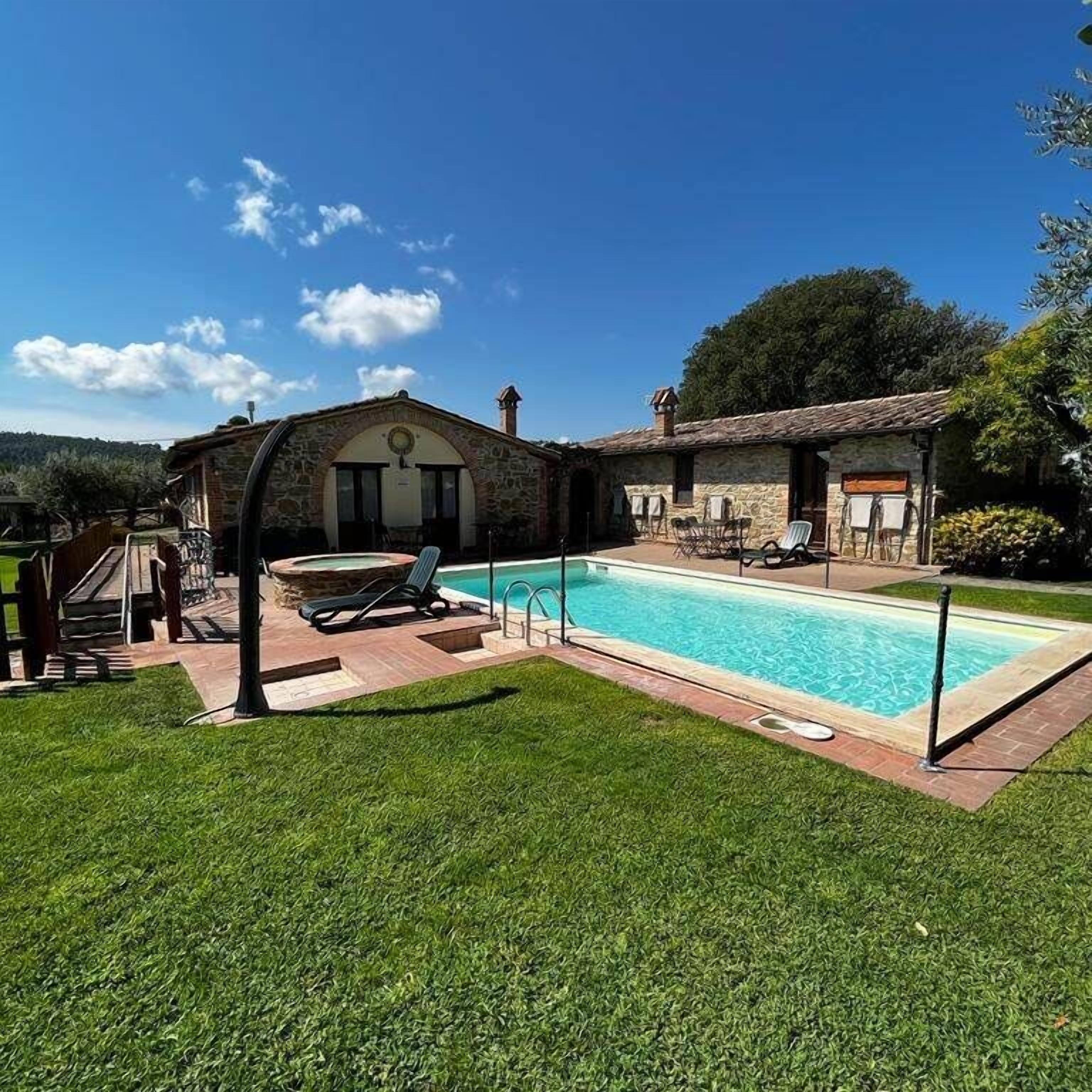 A pool area with a stone building, a hot tub, and lounge chairs.