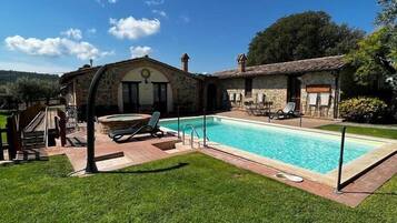A pool area with a stone building, a hot tub, and lounge chairs.