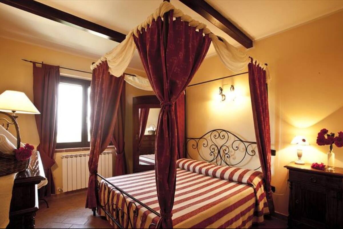 A four-poster bed with striped bedding, a nightstand with a lamp, and a window with curtains.