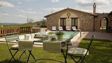 A stone building with a pool, outdoor seating, and a view of the countryside.
