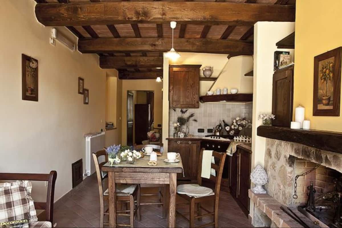 A cozy kitchen with wooden beams, a fireplace, and a dining area with a table set for two.