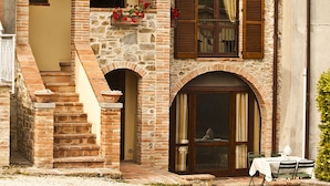 A two-story stone building with a tiled roof, wooden shutters, and a small outdoor seating area with a table and chairs. - Agriturismo Ripaiani (Marsciano)