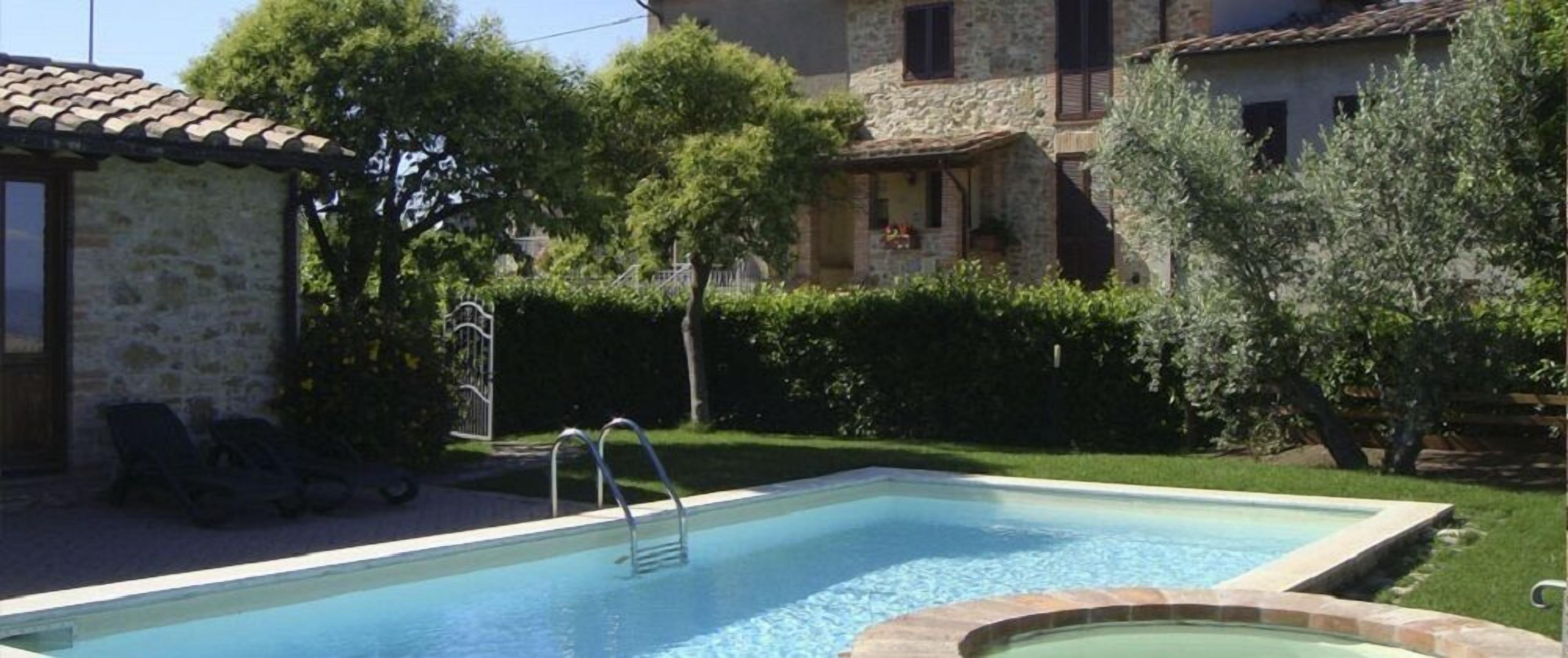 A rectangular swimming pool with a metal ladder, surrounded by a stone wall and lush greenery.