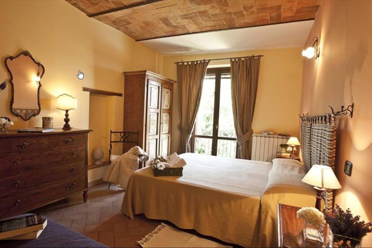 A bedroom with a large bed, wooden dresser, and a mirror. There is a window with curtains and a view of the outdoors.