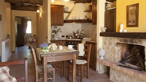A cozy kitchen with wooden furniture, a stone fireplace, and a dining area with a table set for two. - Agriturismo Ripaiani (Marsciano)