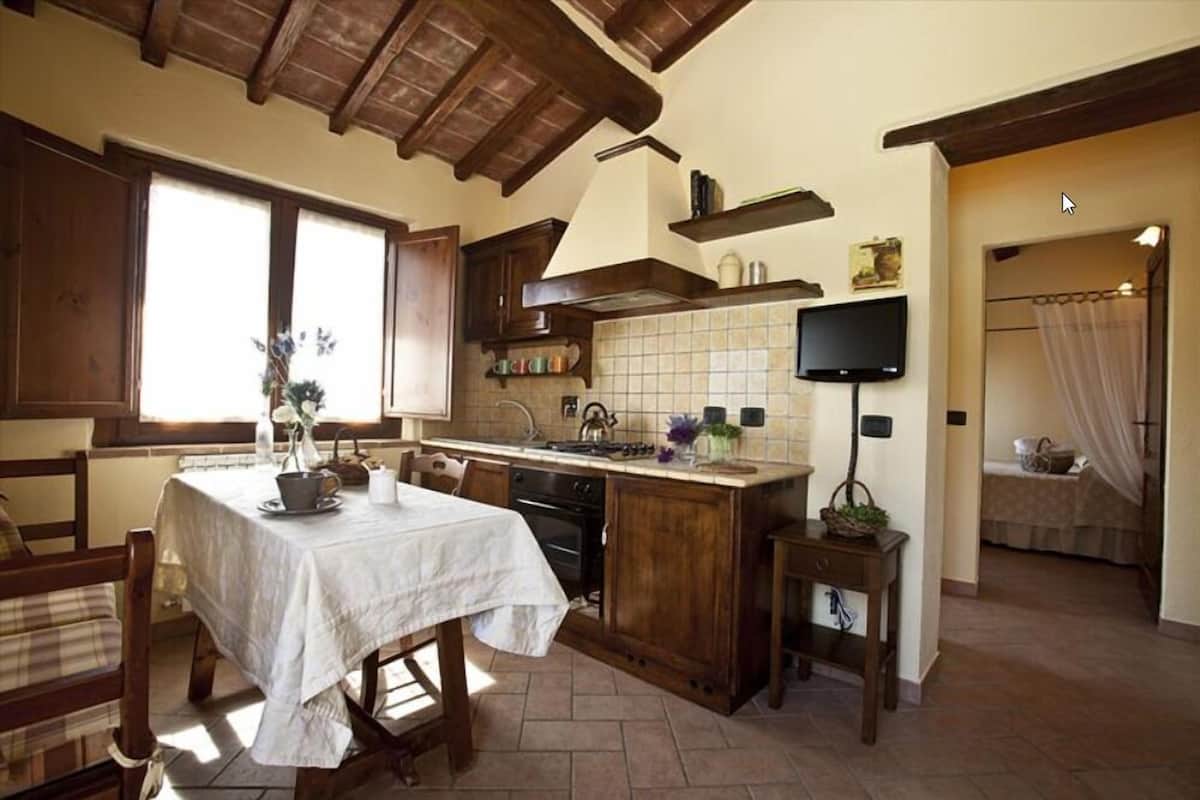 A kitchen with wooden cabinets, a tiled backsplash, a dining table with chairs, and a television mounted on the wall.