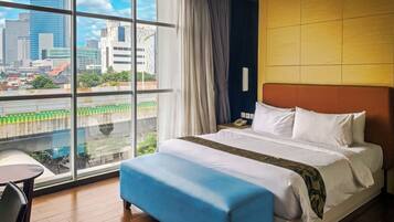 A hotel room with a large window, a bed, a blue bench, and a small table.