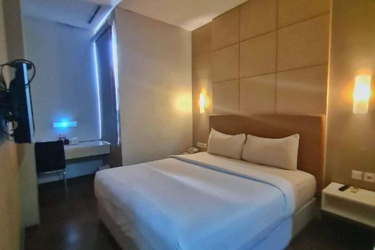 Une chambre d’hôtel comprenant un lit, une table de chevet, une lampe et un bureau avec une chaise.