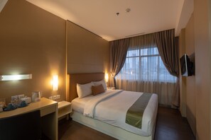 Ein Hotelzimmer mit einem großen Bett, Nachttischen, einem Schreibtisch mit Stuhl, einem Fernseher und einem Fenster mit Vorhängen.