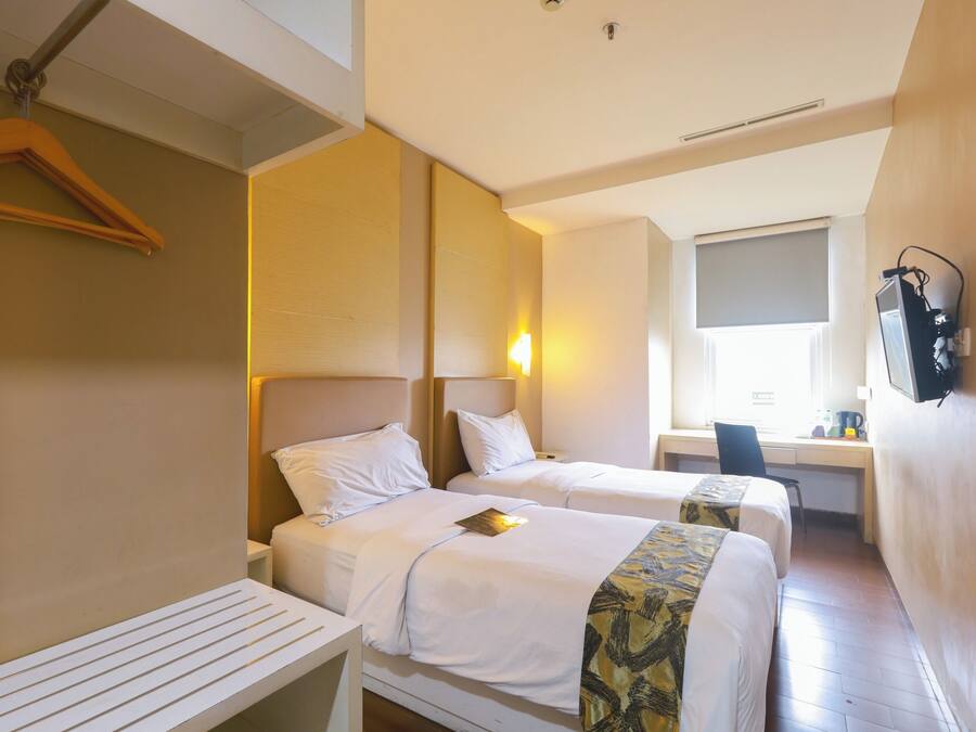 A hotel room with two beds, a desk, a chair, and a TV mounted on the wall.