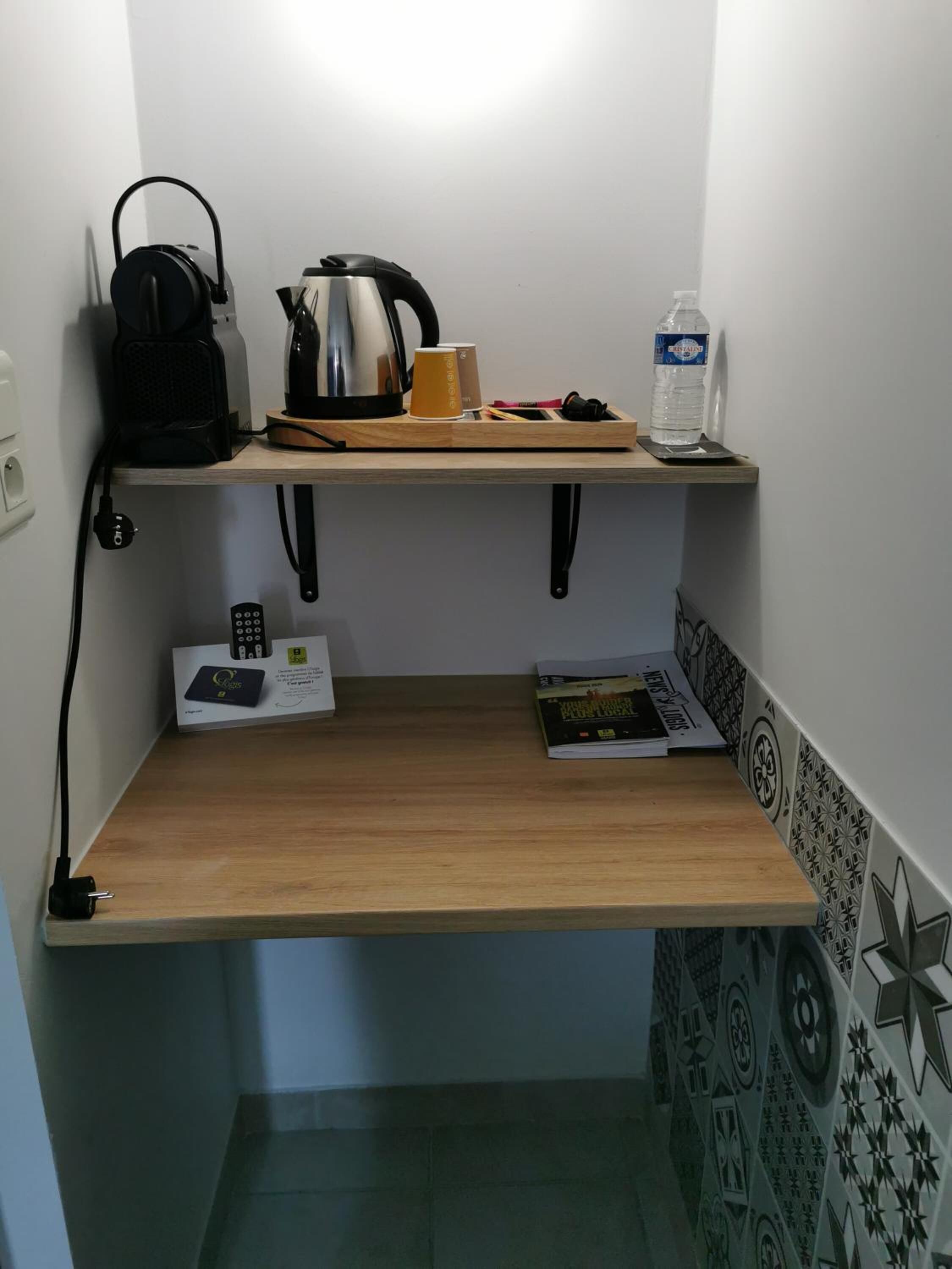 Ett litet pentry med en kaffebryggare, en vattenkokare och en vattenflaska på en hylla.