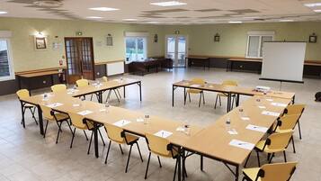 Une salle de conférence équipée de plusieurs tables et chaises, d’un tableau blanc et d’un écran de projection.