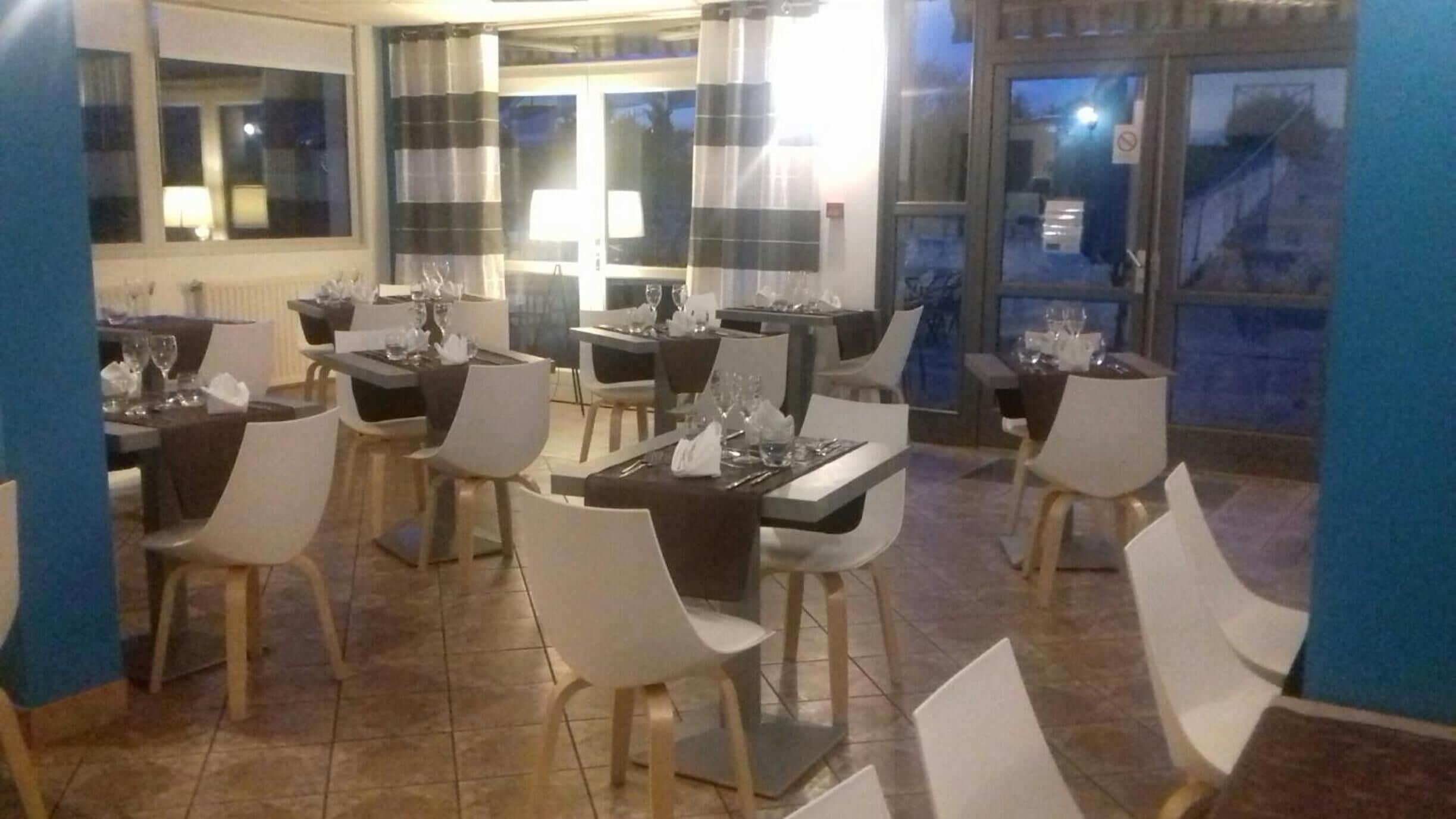 A restaurant with multiple tables and chairs, large windows, and a tiled floor.