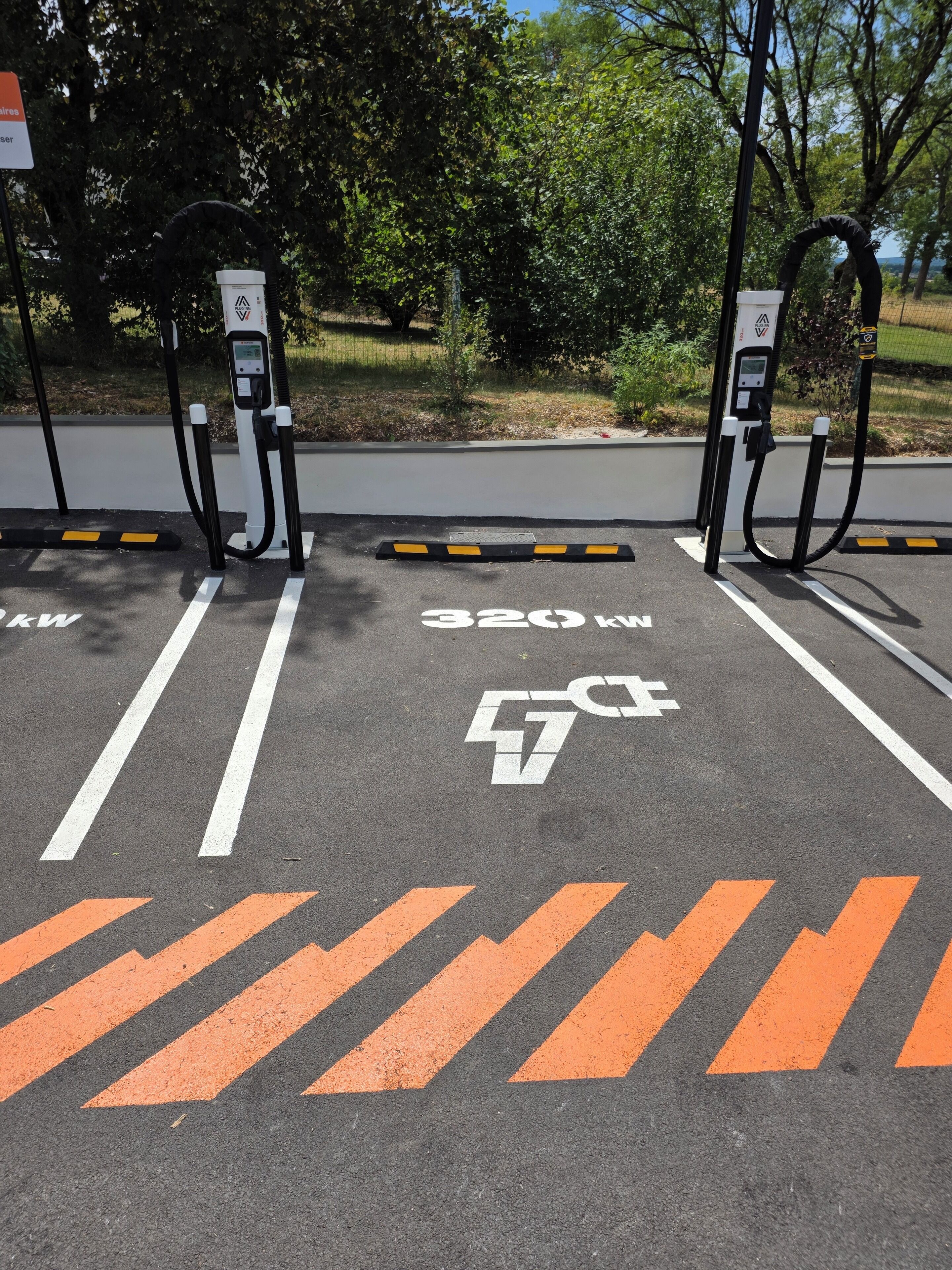 Un área de estacionamiento con estaciones de carga para vehículos eléctricos, carriles señalizados y un letrero que indica una potencia de 320 kW.