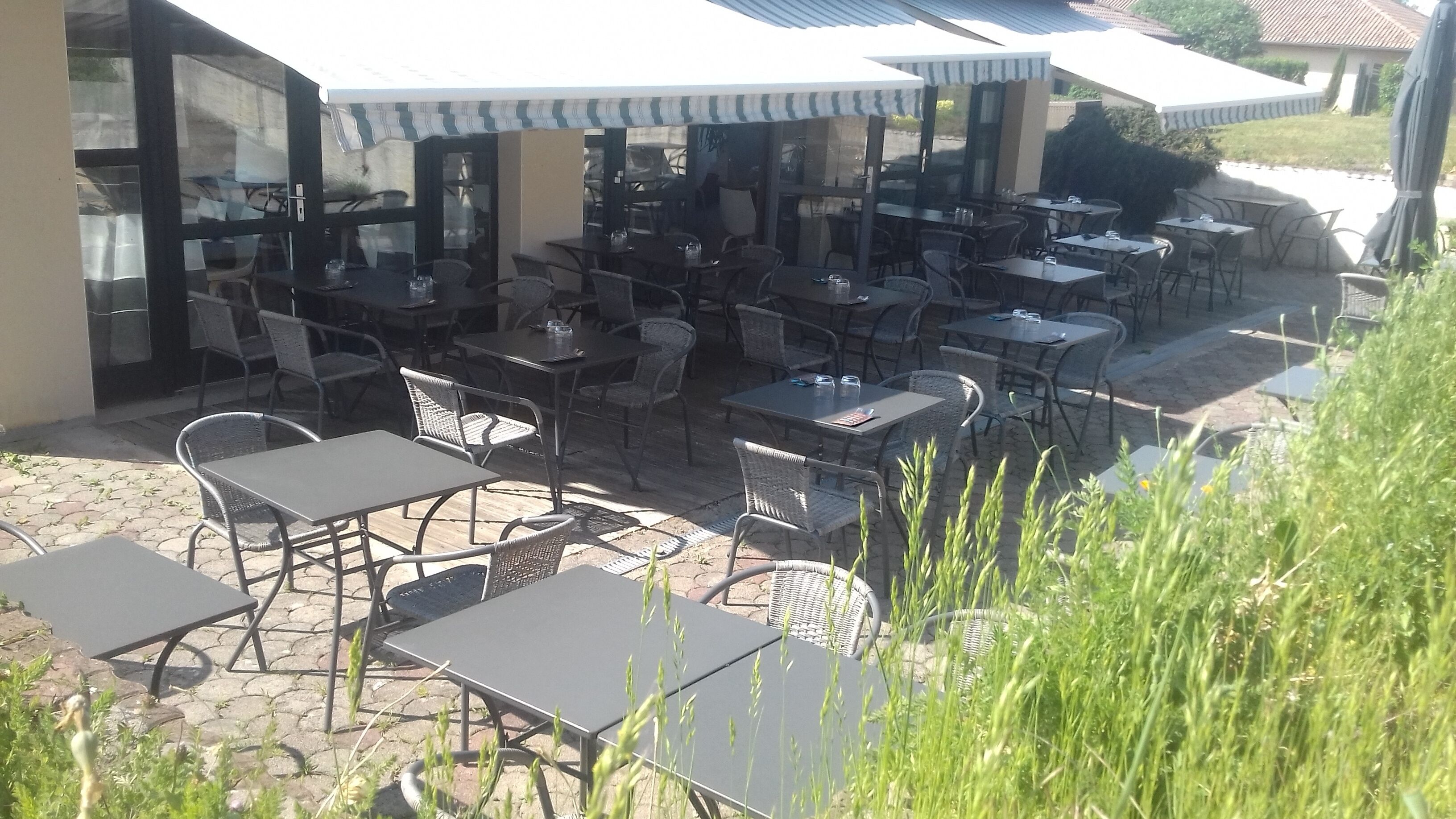 Eine Terrasse im Freien mit mehreren Tischen und Stühlen, von denen einige mit Sonnenschirmen beschattet werden, und einem gepflasterten Boden.