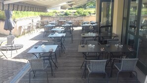 Un patio al aire libre con varias mesas y sillas, una terraza de madera y una puerta de cristal que da al interior.