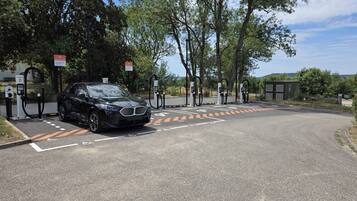 A black car parked at a charging station with trees and a clear sky in the background.