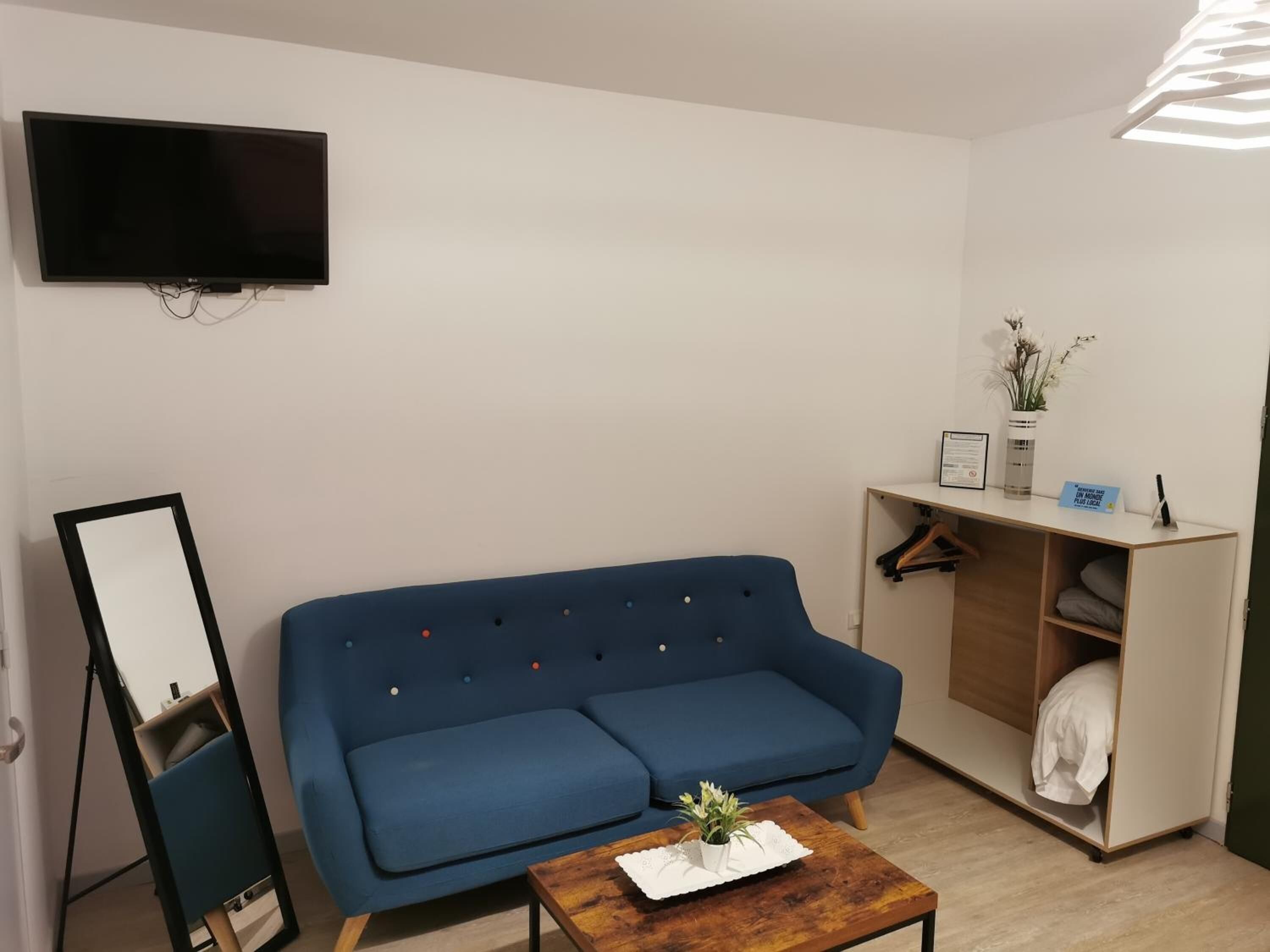 Een moderne woonkamer met een blauwe bank, een klein houten bijzettafeltje, een flatscreen televisie aan de muur en een inbouwkast met een kapstok.