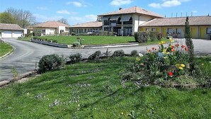 Un hotel con un edificio central y varias estructuras más pequeñas, rodeado de céspedes cuidados y parterres de flores.