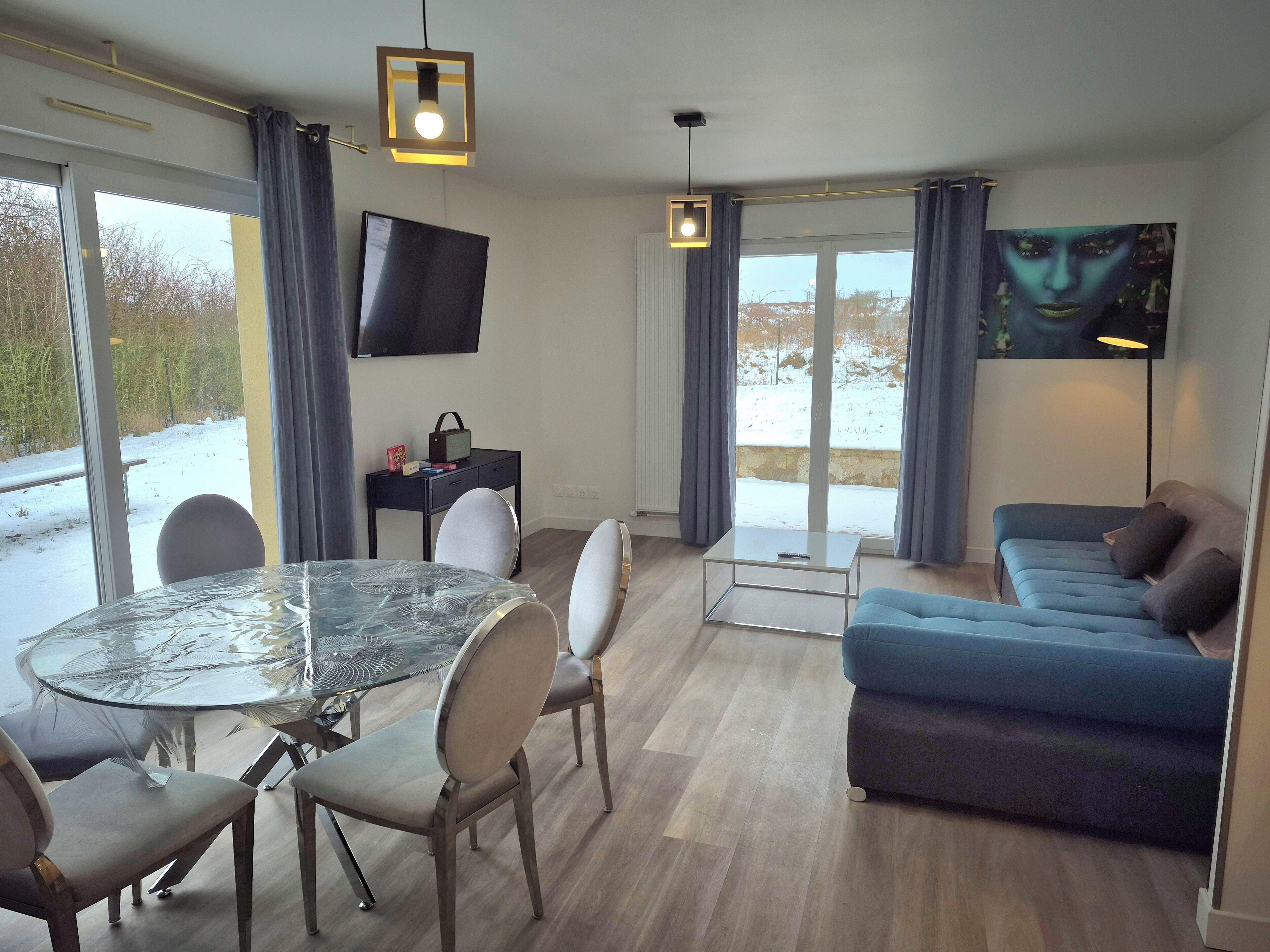 Una sala moderna con una mesa de comedor de vidrio, un sofá azul y un televisor de pantalla plana montado en la pared.
