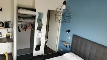 A modern hotel room with a bed, a desk, a wardrobe, and a bathroom visible through an open door.