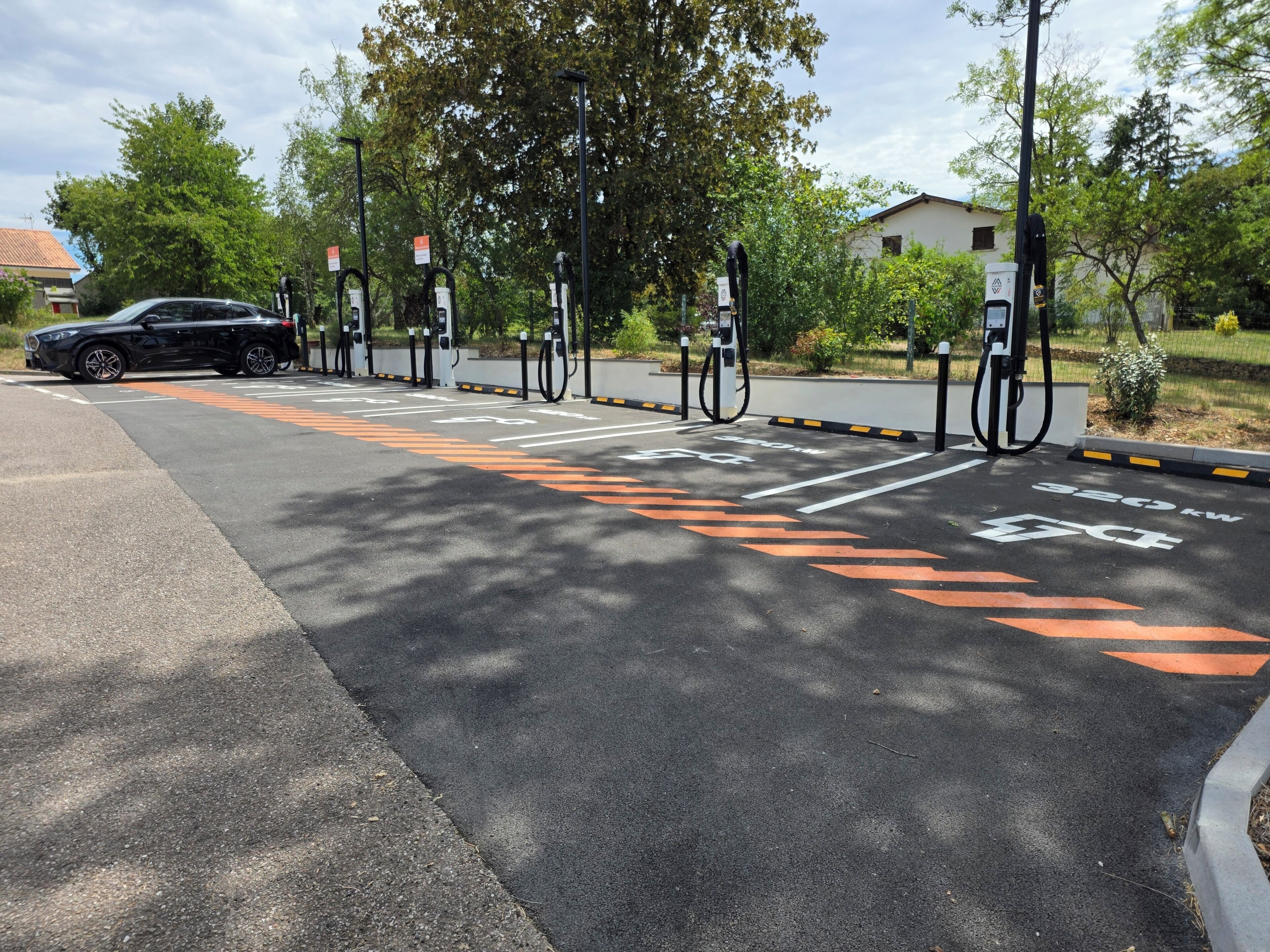 Un área de estacionamiento con estaciones de carga para vehículos eléctricos, espacios delimitados y un automóvil.