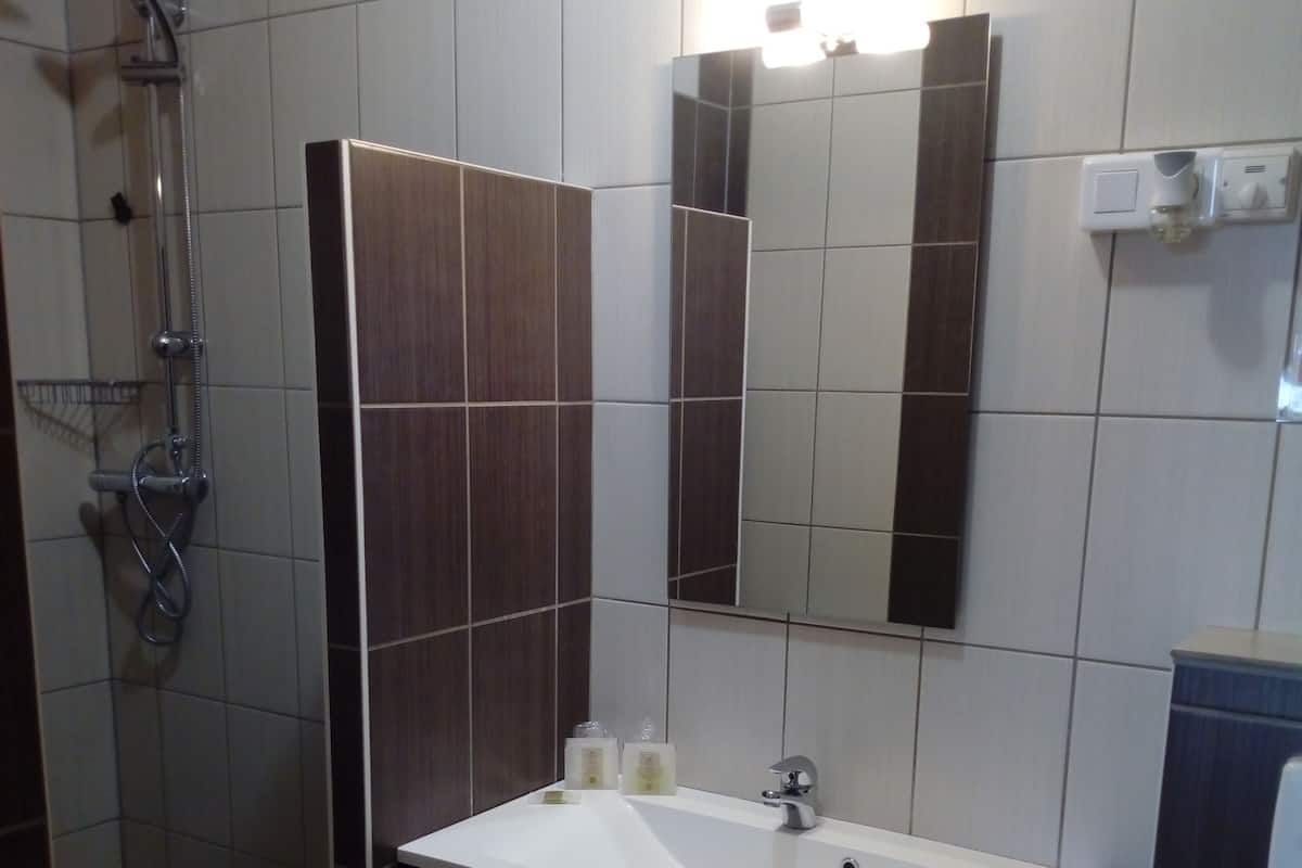 Casa de banho com lavatório branco, espelho, toalha e chuveiro.