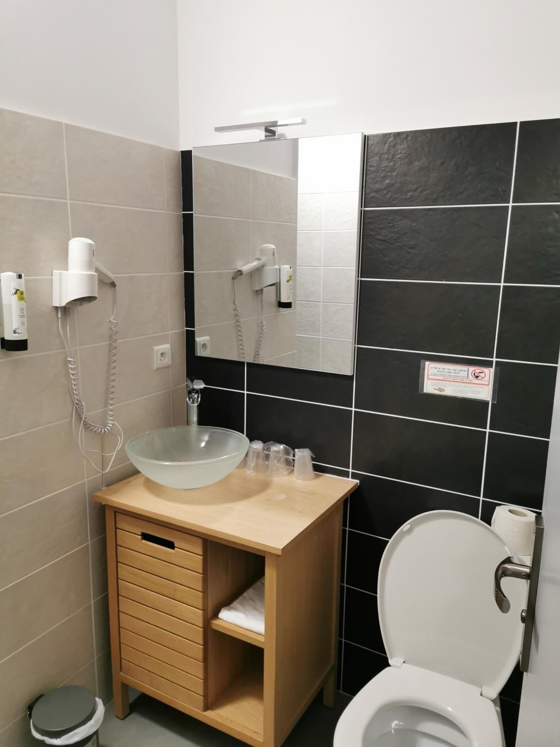 A modern bathroom with a beige vanity, a glass sink, a toilet, and a mirror.