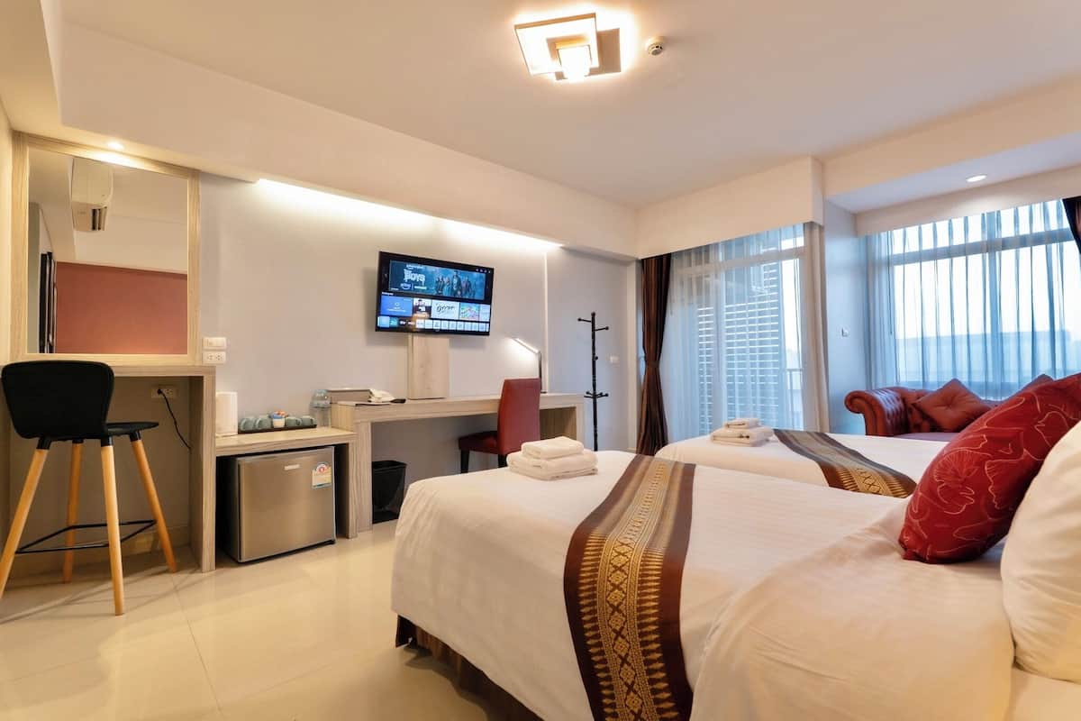 A hotel room with a bed, a desk with a computer, a television, and a window with curtains.