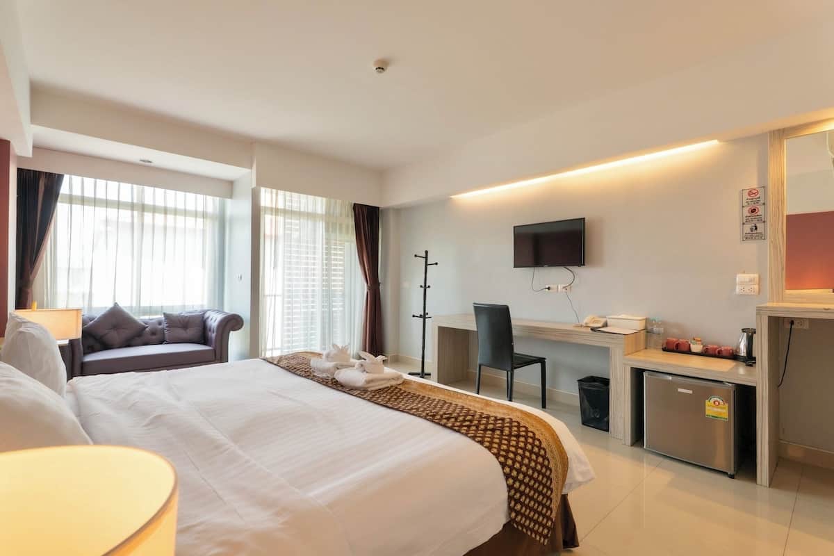 A hotel room with a large bed, a desk, a chair, a television, and a small refrigerator.