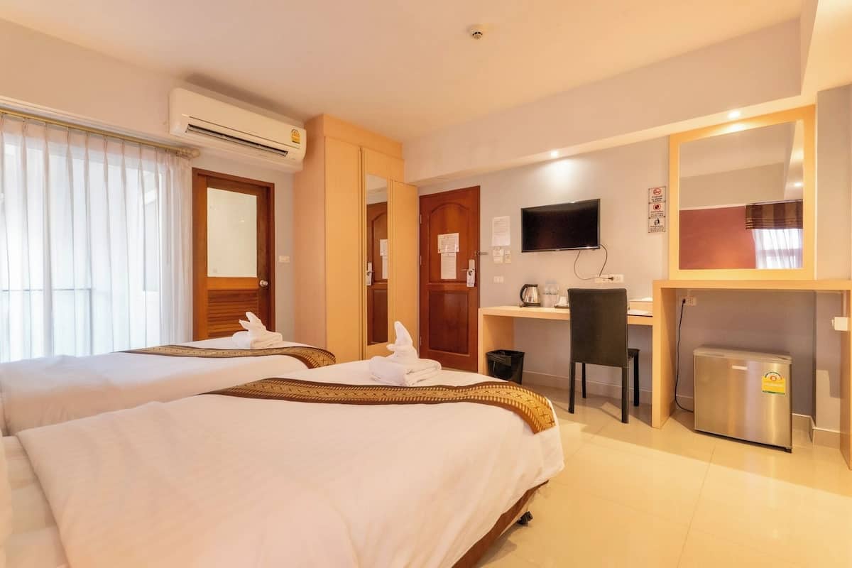 A hotel room with two beds, a desk, a television, and a refrigerator.