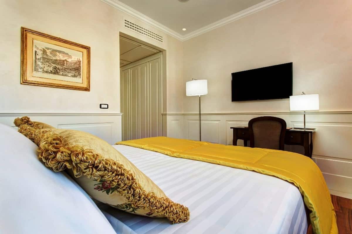 A hotel room with a large bed, two bedside lamps, a flat-screen TV, and a framed picture on the wall.