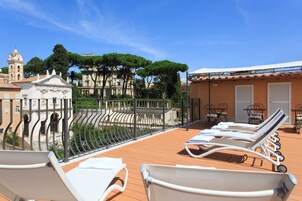 Una terrazza sul tetto con lettini, una ringhiera in ferro battuto e vista su edifici storici e alberi.
