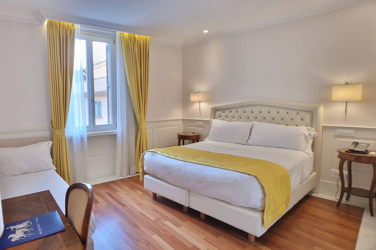 A hotel room with a bed, bedside tables, a desk with a lamp, a chair, and a TV mounted on the wall.