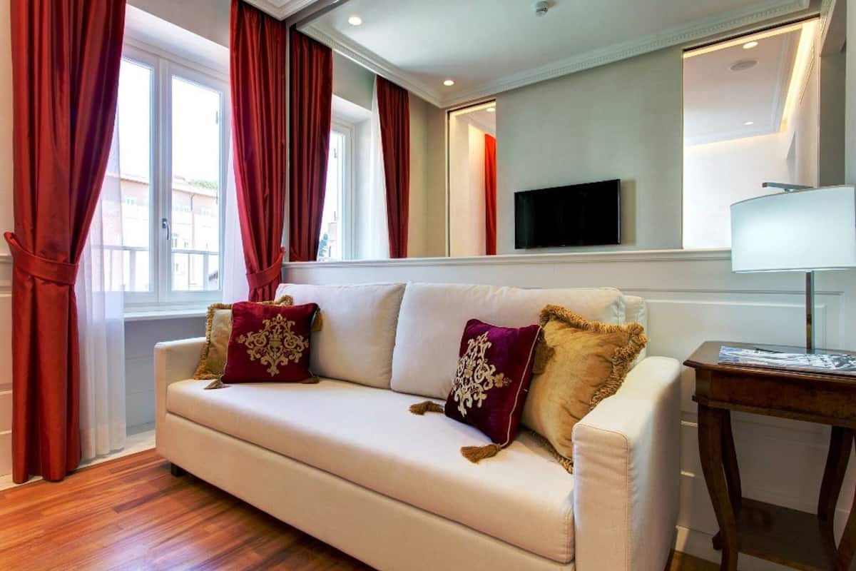 A modern living room with a beige sofa, red curtains, a flat-screen TV, and a lamp on a wooden side table.