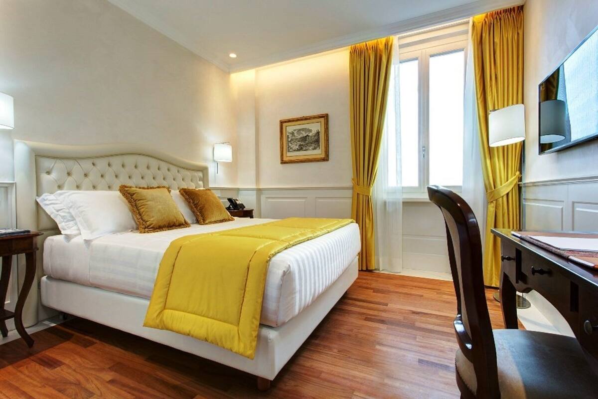 A hotel room with a bed, a desk, a chair, a television, and a window with curtains.