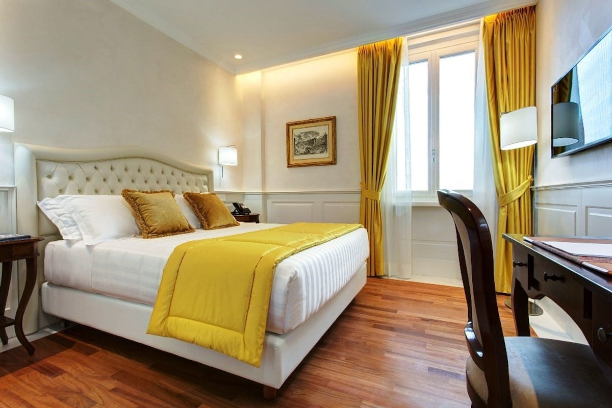 A hotel room with a bed, a desk, a chair, a television, and a window with curtains.