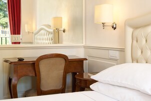 Et hotelværelse med en seng, et skrivebord, en stol og to væglamper.