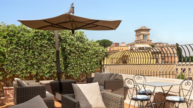 An outdoor seating area with wicker furniture and a table, overlooking a cityscape with a tower. - Hotel degli Artisti (Rome)