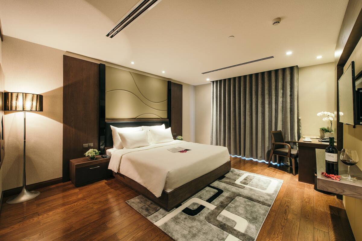 Ein modernes Hotelzimmer mit einem großen Bett, einem Nachttisch, einer Lampe und einem Schreibtisch mit Stuhl.