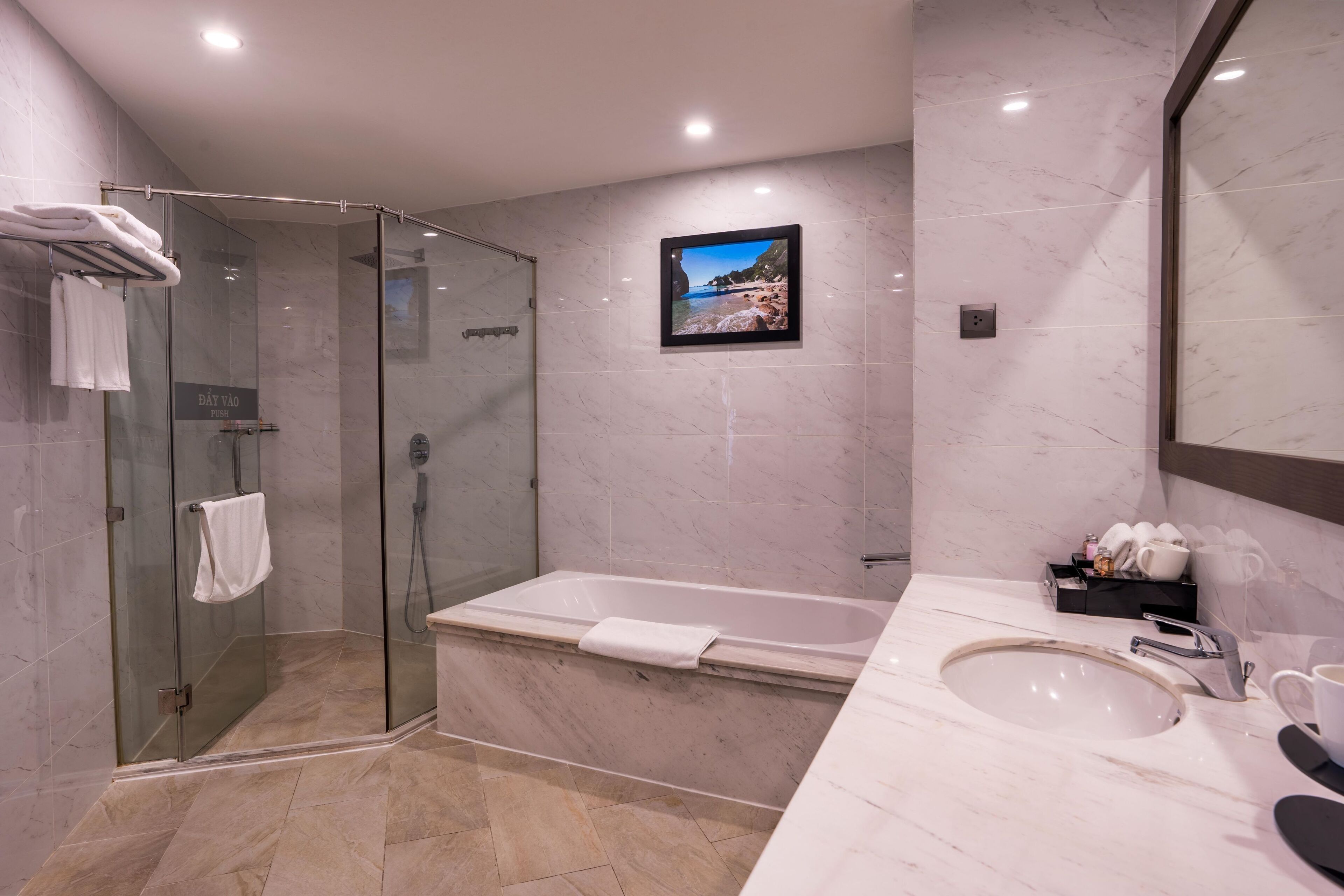 Un baño moderno con ducha envuelta en vidrio, una bañera amplia, un lavamanos y un cuadro en la pared.