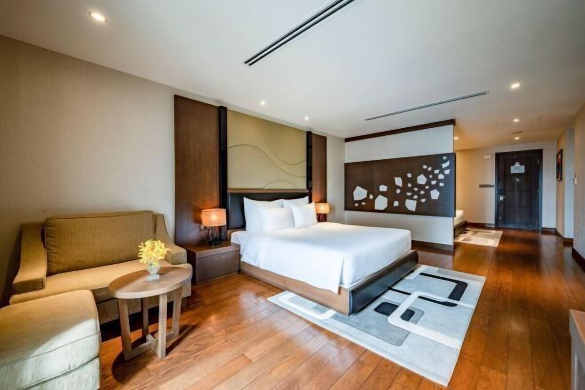 Ein modernes Hotelzimmer mit einem großen Bett, einer Couch, einem kleinen Tisch mit einer Vase und einem Wanddekor.