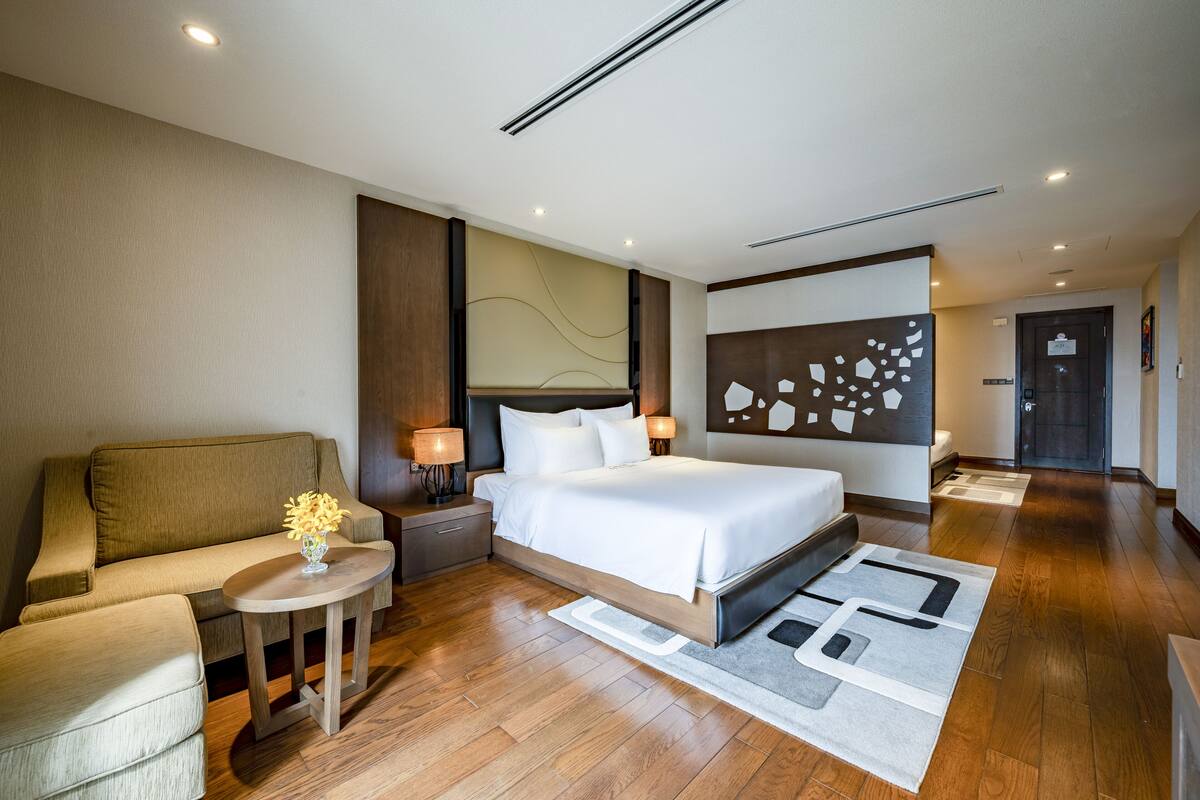 Ein modernes Hotelzimmer mit einem großen Bett, einer Couch, einem kleinen Tisch mit einer Vase und einer dekorativen Wandgestaltung.