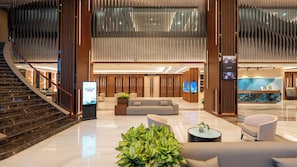 A modern lobby with a staircase, seating area, reception desk, and a large screen.